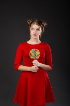 Portrait of a smiling young beautiful girl in a red dress with a big candy. Funny girl with a lollipop