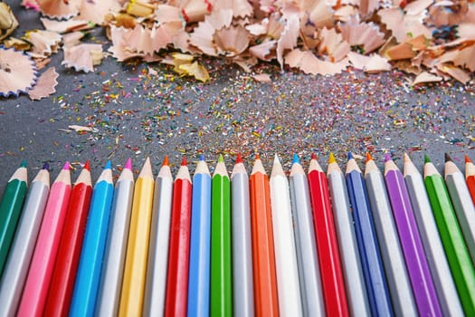 close up shot of colored pencil crayons and pencil crayons shavings on dark background. Sharpened colored pencils