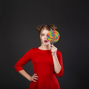 Portrait of a smiling young beautiful girl in a red dress with a big candy. Funny girl with a lollipop