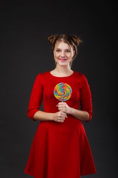 Portrait of a smiling young beautiful girl in a red dress with a big candy. Funny girl with a lollipop