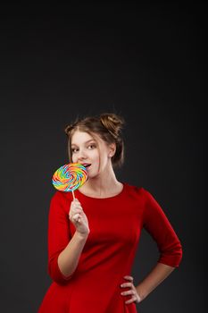 Portrait of a smiling young beautiful girl in a red dress with a big candy. Funny girl with a lollipop