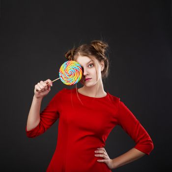 Portrait of a smiling young beautiful girl in a red dress with a big candy. Funny girl with a lollipop