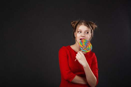 Portrait of a smiling young beautiful girl in a red dress with a big candy. Funny girl with a lollipop