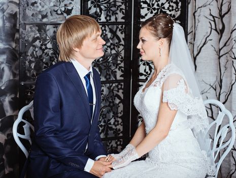 Bride and groom sitting in studio with vintage interior. Photo of happy newlyweds