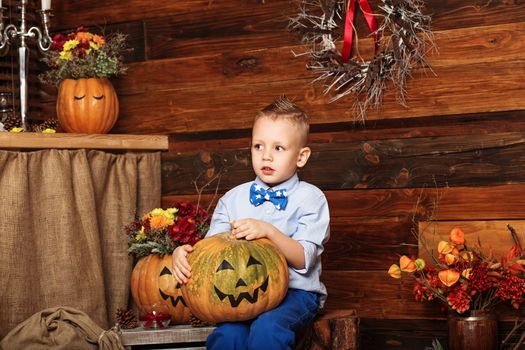 Halloween party with child holding painted pumpkin. Cute Little Boy having fun in Halloween decorations