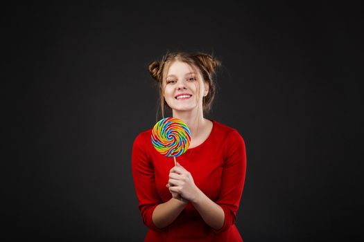 Portrait of a smiling young beautiful girl in a red dress with a big candy. Funny girl with a lollipop
