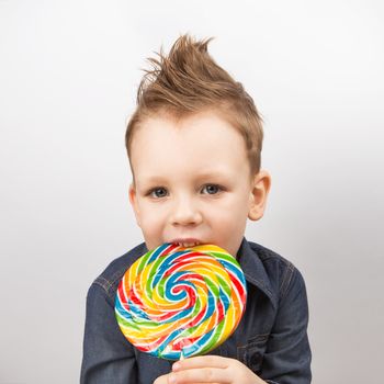 A boy in a denim shirt eating lollipop. Happy kid with a big candy isolated on white background