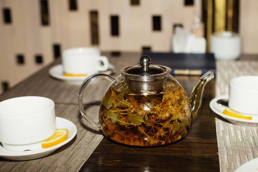 Glass teapot and cups with herbal tea on wooden table. Teapot and cups with linden tea. herbal tea with aroma fresh herb