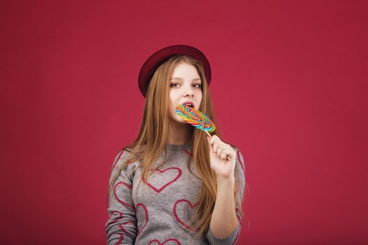 beautiful girl wearing hat biting big striped lollipop