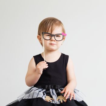 Portrait of a lovely little girl with funny photo props paper glasses against a white background