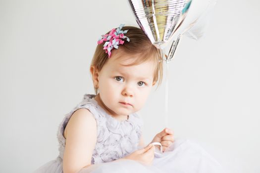 Portrait of a lovely little girl wearing elegant gray dress in front of a white background. Little princess. Little baby girl holding silver star-shaped balloon.
