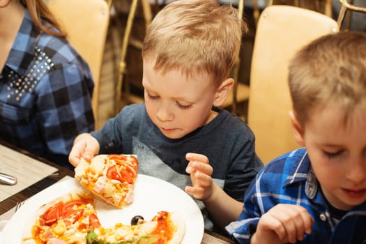 Children eat Italian pizza in the cafe. Adorable little boy eating pizza at a restaurant