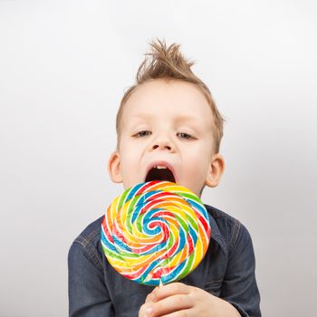 A boy in a denim shirt eating lollipop. Happy kid with a big candy isolated on white background