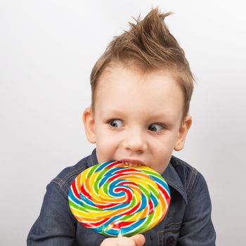 A boy in a denim shirt eating lollipop. Happy kid with a big candy isolated on white background