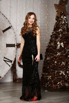 full-length Portrait of a beautiful long-haired young girl in black Evening Dress in interior with Christmas decorations
