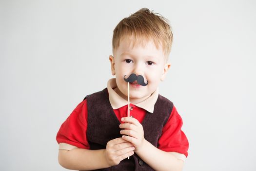 Portrait of a cute little boy with funny photo props paper mustache against a white background