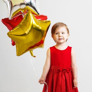 Little baby girl holding balloons in the form of stars. Young girl holding a star-shaped balloons. Happy child with colorful shiny foil balloons against a white background