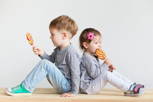 Little children eating lollipops. Happy kids with a big candy. Portrait of a happy little children - boy and girl. Beautiful kids against a white background