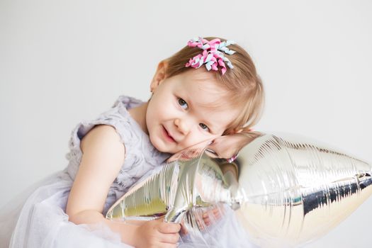 Portrait of a lovely little girl in elegant gray dress in front of a white background. Little princess. Little baby girl playing with silver star-shaped balloon.