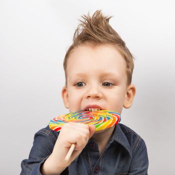 A boy in a denim shirt eating lollipop. Happy kid with a big candy isolated on white background