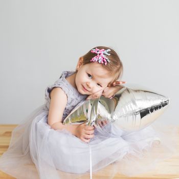 Portrait of a lovely little girl in elegant gray dress in front of a white background. Little princess. Little baby girl playing with silver star-shaped balloon.