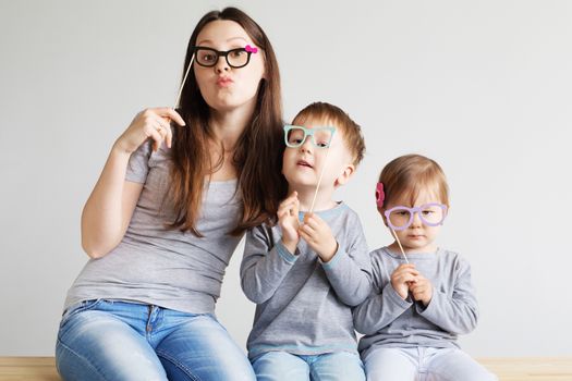 Portrait of a happy mother and her two little children - boy and girl. Happy family with funny photo props cardboard glasses against a white background