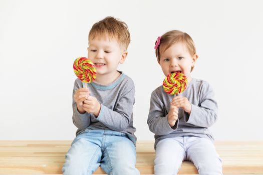Little children eating lollipops. Happy kids with a big candy. Portrait of a happy little children - boy and girl. Beautiful kids against a white background