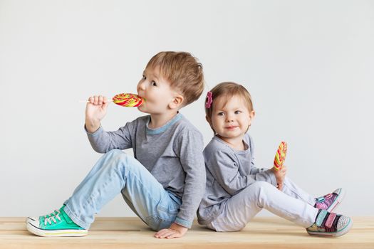 Little children eating lollipops. Happy kids with a big candy. Portrait of a happy little children - boy and girl. Beautiful kids against a white background