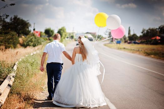 Happy married couple with balloons walk together on the road