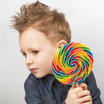 A boy in a denim shirt eating lollipop. Happy kid with a big candy isolated on white background