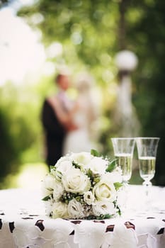 Wedding bridal bouquet with white roses on the table in the garden against the background of the bride and groom. Wedding concept