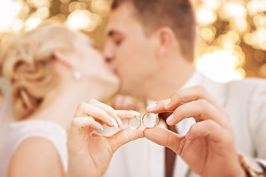 Two gold wedding rings on arms of kissing newlyweds. Small depth of field.