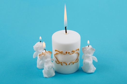 White Souvenir gift candles in the shape of angels. A burning candle on blue background. Candle lit. White Easter candles