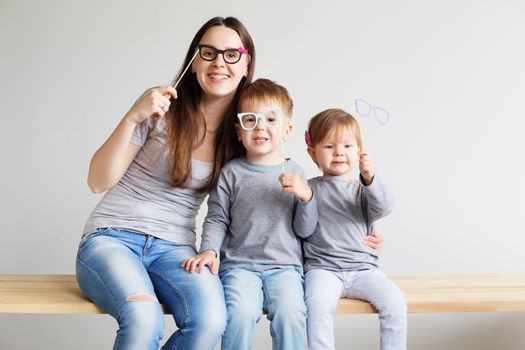 Portrait of a happy mother and her two little children - boy and girl. Happy family with funny photo props cardboard glasses against a white background