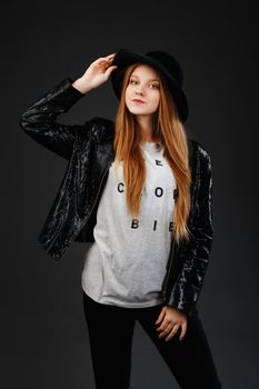 Portrait of beautiful young girl wearing black felt hat and leather jacket in front of a dark gray background