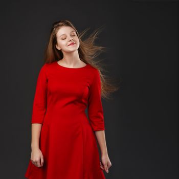 Portrait of a young beautiful girl with eyes closed in a red dress with a flying hair. Girl with long flowing hair. Hair fluttering in motion.