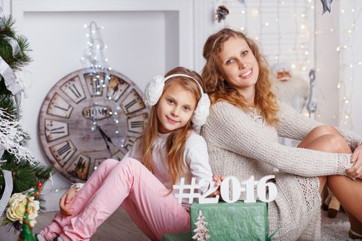 Portrait of happy smiling little girl with mother sitting among Christmas decorations