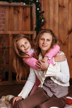 Portrait of happy smiling little girl with mother sitting among Christmas decorations