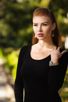 Portrait of beautiful sexy urban girl walking in city park. Portrait of a young gorgeous redhead girl in black clothing. Gorgeous girl with puffy lips natural