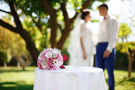Wedding bridal bouquet with pink and white flowers on the table in the garden against the background of the bride and groom. Wedding concept