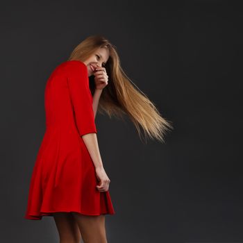 Portrait of a laughing young beautiful girl in a red dress with a flying hair. Girl with long flowing hair. Hair fluttering in motion. Back view