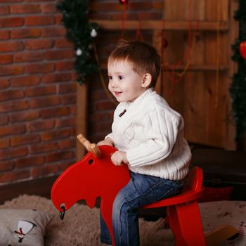 Portrait of a cute little boy. Little boy among Christmas decorations. Boy riding a rocking deer. Rocking deer chair for kids ride playing