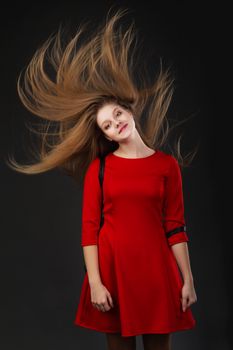Beautiful girl with hair motion freeze over gray background. Blonde woman with her lond hair blowing looking at camera. The concept of hair care products. Healthy long shiny hair