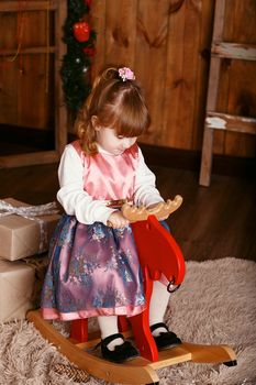 Portrait of a lovely little girl. Portrait of cute little girl among Christmas decorations. Girl riding a rocking deer. Rocking deer chair for kids ride playing