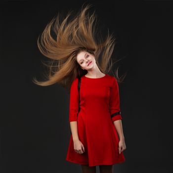 Portrait of a smiling young beautiful girl in a red dress with a flying hair. Girl with long flowing hair. Hair fluttering in motion.