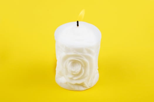 Carved white candle on yellow background. Souvenir gift candle in the shape of rose. Candle lit. St. valentine's day.