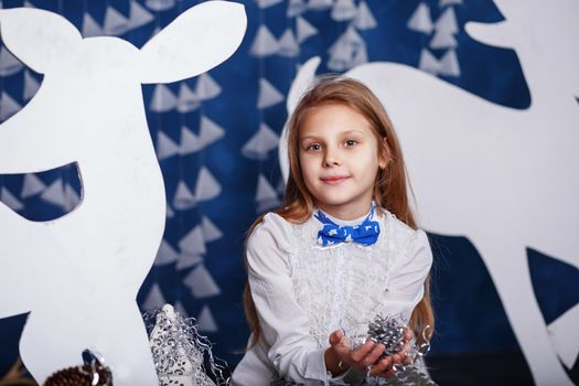 Little girl with bow-tie in christmas decorations. Portrait of Beautiful little girl with long blond hair. Decor winter forest.