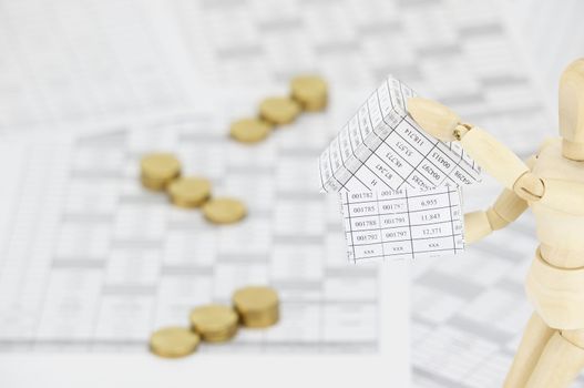 Wooden dummy holding house on finance account have blur step pile of gold coins as background.