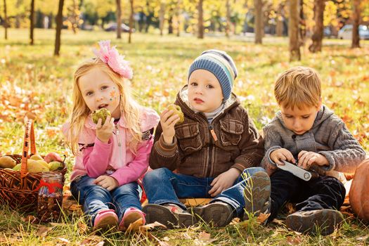 Three happy children playing in autumn park with fruits