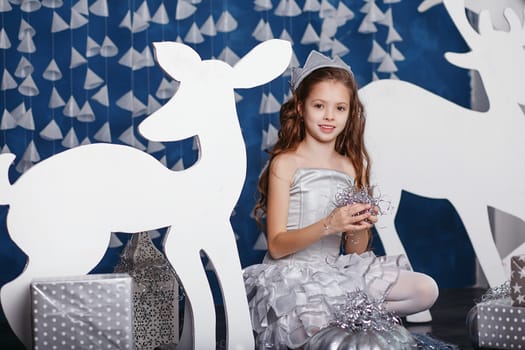 Little girl in christmas decorations. Portrait of Beautiful little girl with long curly hair with crown. Decor winter forest. Little Princess